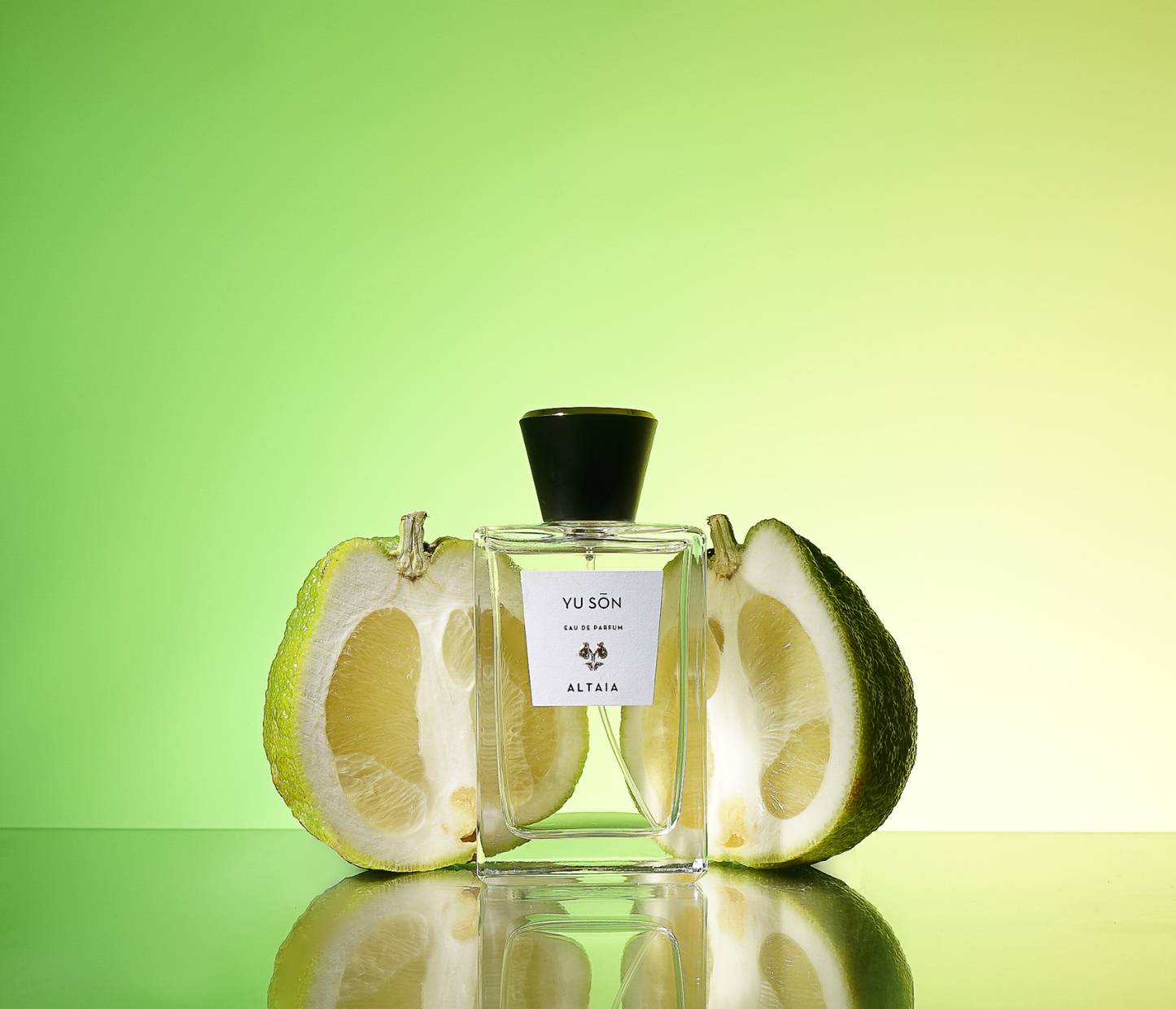 Altaia Yu Son perfume bottle between a citrus fruit on a green and yellow background.